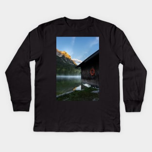 Boathouse with lifesaver Portrait. Amazing shot of a wooden house in the Ferchensee lake in Bavaria, Germany, in front of a mountain belonging to the Alps. Scenic foggy morning scenery at sunrise. Kids Long Sleeve T-Shirt